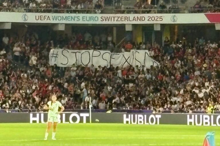 Das Bild zeigt ein Spiel der Frauen Europameisterschaft Schweiz 2025. In den Zuschauerrängen wir dein Banner mit der Aufschrift StopSexismus Hochgehalten.