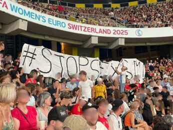 Gemeinsam sichtbar gegen Sexismus! Das Bild zeigt ein Spiel der Frauen Europameisterschaft Schweiz 2025. In den Zuschauerrängen wir dein Banner mit der Aufschrift StopSexismus Hochgehalten.