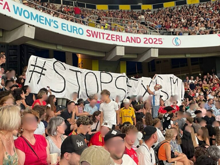 Das Bild zeigt ein Spiel der Frauen Europameisterschaft Schweiz 2025. In den Zuschauerrängen wir dein Banner mit der Aufschrift StopSexismus Hochgehalten.